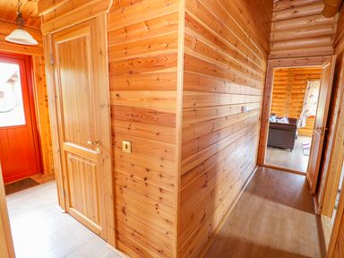 A wooden hallway with doors leading to other rooms and a view of a living area with a sofa at Willow Lodge in Greetham Rutland