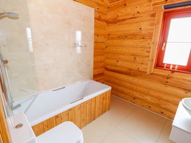 A bathroom with a bathtub a toilet and a window in a wooden cabin at Willow Lodge in Greetham Rutland