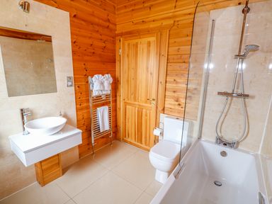 A bathroom with a white sink, toilet, bathtub with shower, towel rack, and wooden walls at Willow Lodge in Greetham Rutland