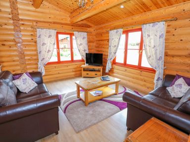 A sitting room with two leather sofas a coffee table a television and floral curtains at Willow Lodge in Greetham Rutland