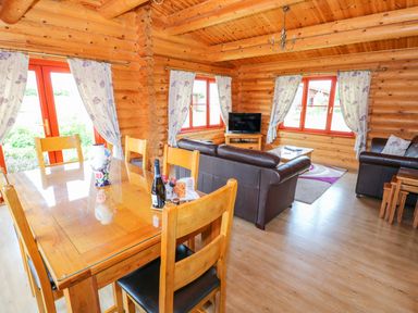 A dining area with wooden table and chairs and a living room with leather sofas and a television in a log cabin at Willow Lodge in Greetham Rutland