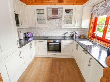 A kitchen with white cabinets a black countertop a purple toaster and kettle near a window at Willow Lodge in Greetham Rutland