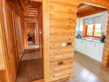 A wooden hallway leading to a bedroom and a kitchen with white cabinets and a window at Willow Lodge in Greetham Rutland