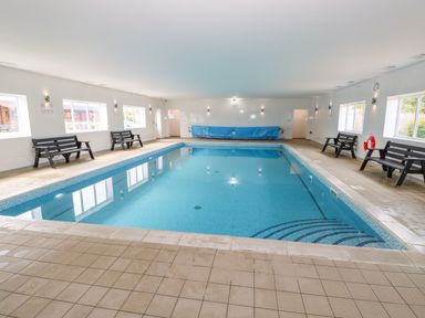 An indoor swimming pool with tiled floor benches along the sides and windows on the walls at Willow Lodge in Greetham Rutland