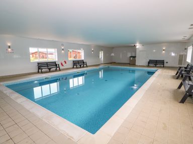 An indoor swimming pool with benches along the walls and windows showing wooden buildings outside at Willow Lodge in Greetham Rutland