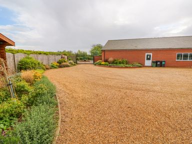 A gravel driveway with garden beds along the sides and a brick building at the end at Willow Lodge in Greetham Rutland