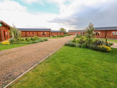 A courtyard with gravel paths surrounded by wooden lodges and green lawns at Willow Lodge in Greetham Rutland
