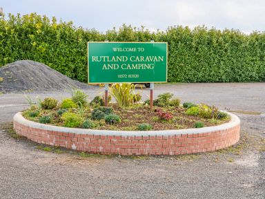 A green welcome sign for Rutland Caravan and Camping on a circular brick planter with plants and gravel ground
