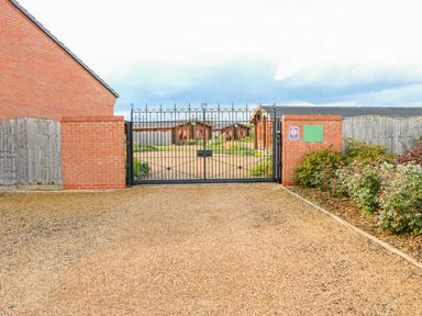 A gate entrance with brick pillars opening to gravel pathway and wooden buildings behind at Willow Lodge in Greetham Rutland