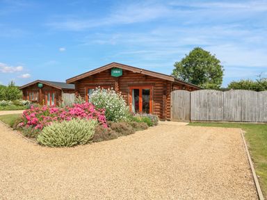 A gravel driveway with flower beds and wooden cabins behind a wooden fence at Willow Lodge in Greetham Rutland