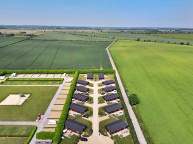 A cluster of small cabins with driveways in a rural area surrounded by green fields at Willow Lodge in Greetham Rutland