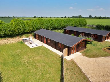 Two long single-storey wooden lodges with patios and outdoor furniture in a rural green field at Willow Lodge in Greetham Rutland