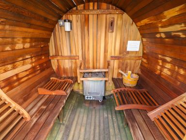 An interior view of a wooden sauna with benches a heater and wooden bucket at Sycamore Lodge in Greetham Rutland