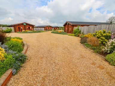 A gravel driveway with several wooden cabins and landscaped flowerbeds at Sycamore Lodge in Greetham Rutland