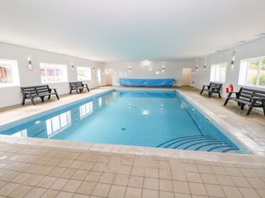 An indoor swimming pool with benches along the sides and windows on the walls at Sycamore Lodge in Greetham Rutland
