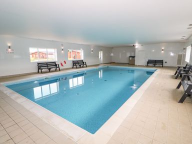 An indoor swimming pool with benches along the walls and windows showing outside cabins at Sycamore Lodge in Greetham Rutland