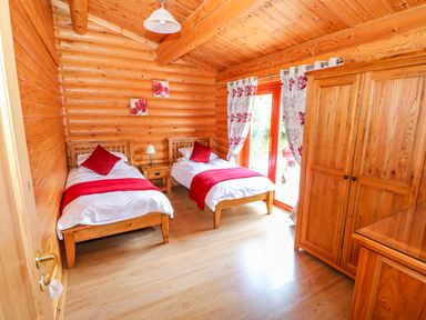 A bedroom with two single beds red pillows and blankets wooden furniture and a door with patterned curtains at Sycamore Lodge in Greetham Rutland