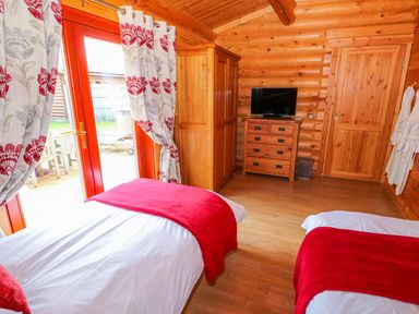 A bedroom with two single beds with red throws wooden wardrobe chest of drawers and TV at Sycamore Lodge Greetham Rutland