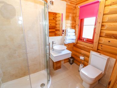 A bathroom with a shower cabin a toilet a sink with a round basin and rolled towels on a towel rack at Sycamore Lodge in Greetham Rutland
