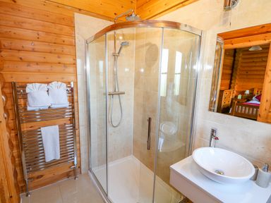A bathroom with a glass shower enclosure a round sink on a white vanity and a towel rack with white towels at Sycamore Lodge in Greetham Rutland