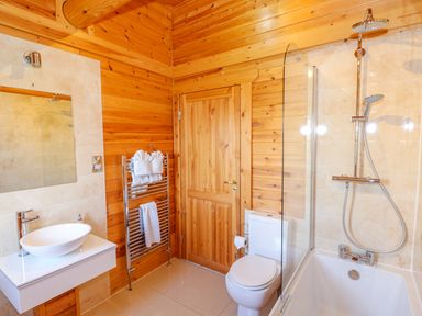 A bathroom with wooden walls a white sink a toilet a bathtub with shower and a towel rack with towels at Sycamore Lodge in Greetham Rutland