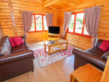 A living room with two brown leather sofas red cushions a wooden coffee table and a television at Sycamore Lodge in Greetham Rutland