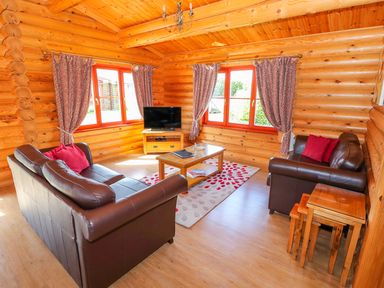 A living room with brown leather sofas a wooden coffee table television and patterned curtains at Sycamore Lodge in Greetham Rutland