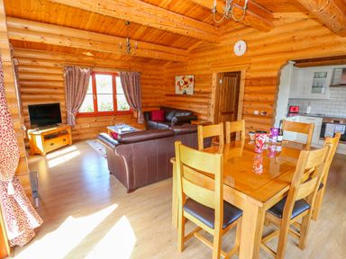 A dining and living area with wooden table and chairs leather sofas and a kitchen in a log cabin at Sycamore Lodge in Greetham Rutland