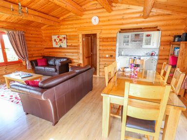 A living room and dining area with brown leather sofas wooden dining table and kitchen at Sycamore Lodge in Greetham Rutland