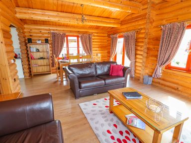 A living room with brown leather sofas wooden coffee table and dining table in a log cabin at Sycamore Lodge in Greetham Rutland