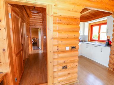 A wooden hallway leading to a bedroom and a kitchen with white cabinets and a red window frame at Sycamore Lodge in Greetham Rutland