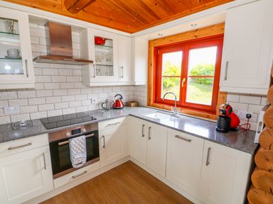 A kitchen with white cabinets a built in oven stovetop a red kettle and coffee machine at Sycamore Lodge in Greetham Rutland
