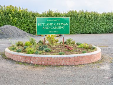 A green sign that says welcome to rutland caravan and camping on a brick circular flower bed in an outdoor parking area