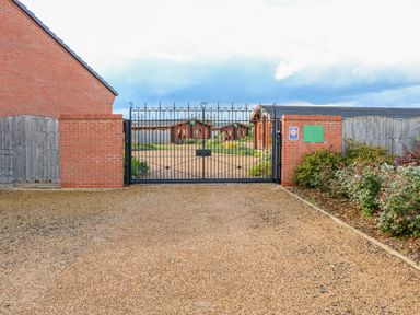 A gated entrance with iron gates and brick pillars leading to wooden lodges at Sycamore Lodge in Greetham Rutland