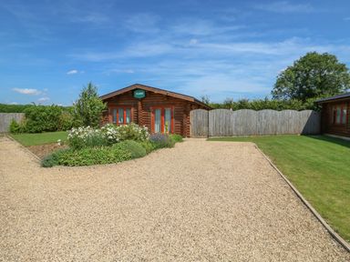 A wooden cabin with a gravel driveway and garden at Sycamore Lodge in Greetham Rutland