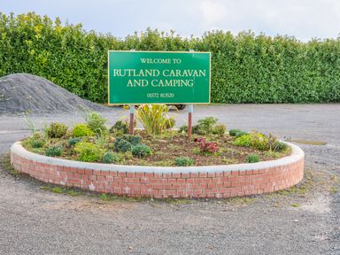 A green welcome sign for Rutland Caravan and Camping in a circular flower bed with plants and gravel ground at Church View in Greetham Rutland