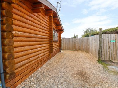 An exterior side view of a log cabin with gravel ground and wooden fencing at Church View in Greetham Rutland