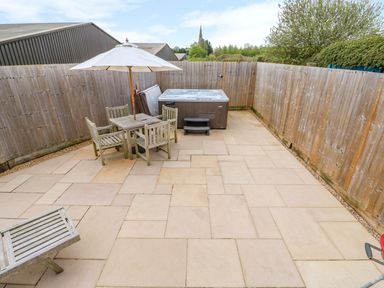 An outdoor patio with a wooden table and chairs under an umbrella a hot tub and a wooden fence around at Church View in Greetham Rutland