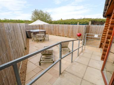 A fenced outdoor patio area with wooden chairs a table with umbrella a hot tub and a red barbecue grill at Church View in Greetham Rutland