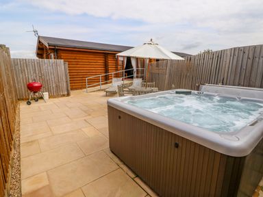 An outdoor patio with a hot tub wooden chairs table and umbrella next to a wooden cabin at Church View in Greetham Rutland