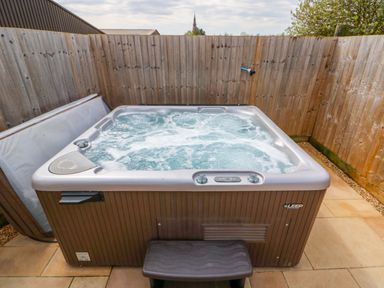 An outdoor hot tub with bubbling water and a small step in a fenced patio area at Church View in Greetham Rutland