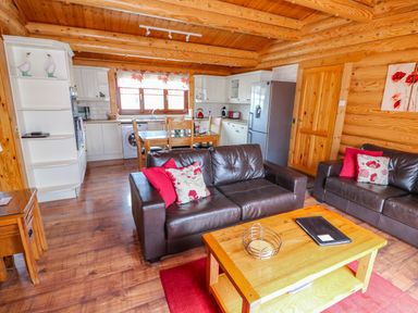 A living area with two brown sofas and a wooden coffee table next to a kitchen with white cabinets and a dining table at Church View in Greetham Rutland
