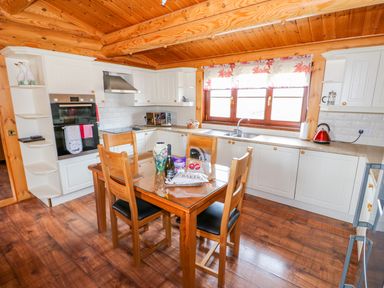 A kitchen with wooden ceiling and floor white cabinets a dining table with four chairs and a window with floral curtains at Church View in Greetham Rutland