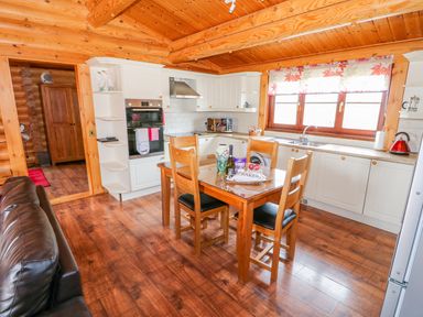 A kitchen with wooden beams white cabinets a dining table with four chairs and a window with floral curtains at Church View in Greetham Rutland