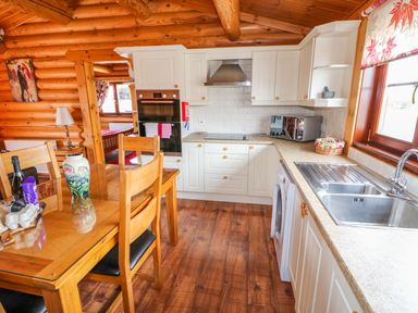 A kitchen with wooden dining table and chairs white cabinets and a sink next to a window at Church View in Greetham Rutland