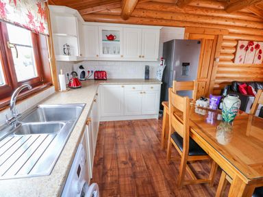A kitchen with a stainless steel sink wooden cabinets red appliances and a wooden dining table with chairs at Church View in Greetham Rutland