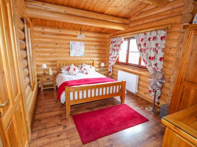 A bedroom with wooden bed and floral curtains in a log cabin at Church View in Greetham Rutland