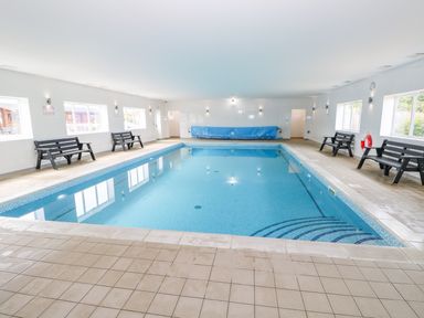 An indoor swimming pool with benches along the walls and windows at Cedar Lodge in Greetham Rutland