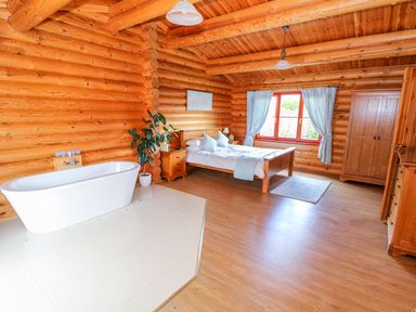 A bedroom with a wooden bed a white bathtub a wooden wardrobe and a plant at Cedar Lodge in Greetham Rutland