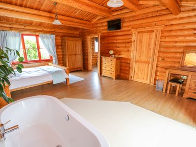 A bedroom with a bed near a window wardrobe dresser and bathtub in a wooden log cabin Cedar Lodge Greetham Rutland